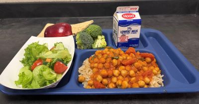 Blue school meal tray with Chickpea Masala, side salad with tomato and carrot, broccoli, apple, pita, milk